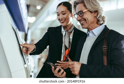 Flight attendant assisting male traveler in doing the self check-in using a machine at the airport terminal. Passenger at self service check in machine with airport female staff. - Powered by Shutterstock