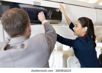 flight attendant helping passenger with carry on luggage to overhead bins