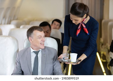 Flight Attendant Serving Water And Cup Of Tea Or Coffee To Businessman Passenger In Airplane