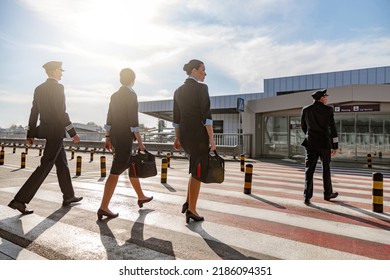 Flight Attendants With Bags And Pilots Crossing The Road In The Airport