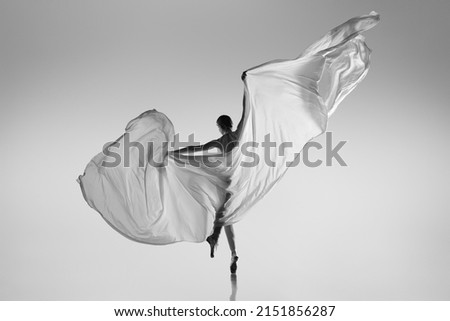 Flight of bird. Black and white portrait of graceful ballerina dancing with fabric, cloth isolated on grey studio background. Grace, art, beauty, contemp dance concept. Weightless, flexible actress