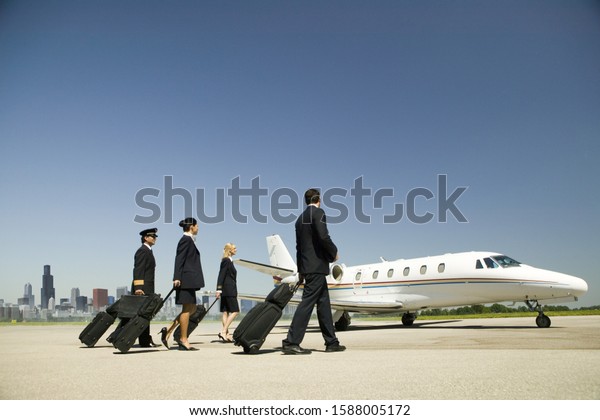 Flight crew\
wheeling suitcases to airplane on\
tarmac