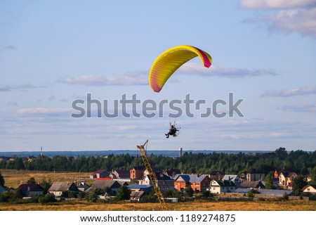 Flight of  motor paraplan.   man flies on  bright colorful motoparaplane above the village, field and construction site.
