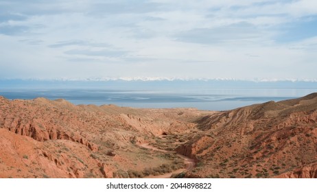 A Flight Over A Big Red Rock With Dry Bushes And The Discovery Of A Wonderful Valley Of Red Rocks With Orange Sand, A Road And A Large Cave Against The Background Of The Great Ten Thousand Glaciers.