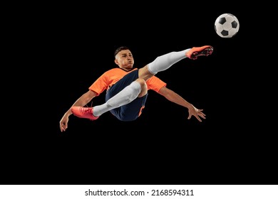 Flight. Portrait of professional male football soccer player in motion isolated on dark background. Concept of sport, goals, competition, hobby, ad. Sportsmen wearing orange-blue football kit