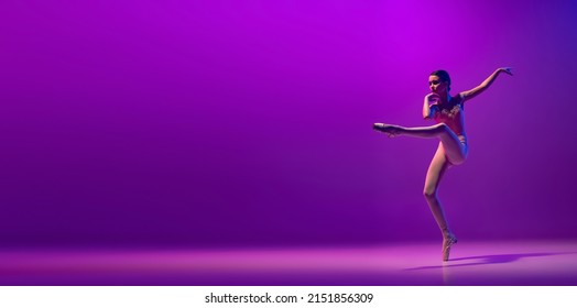 Flight. Portrait of young little ballet dancer, teen jumping isolated on purple background in neon light. Art, grace, beauty, ballet school concept. Copy space for ad - Shutterstock ID 2151856309
