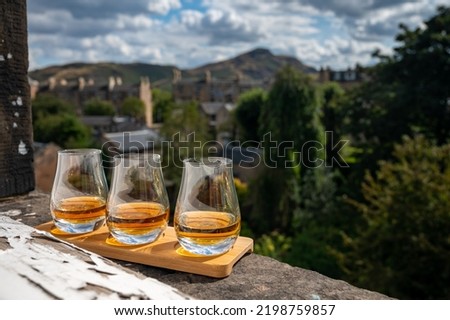 Flight of single malt scotch whisky served on old window sill in Scottisch house with view on old part of Edinburgh city and hills, Scotland, UK, dram of whiskey