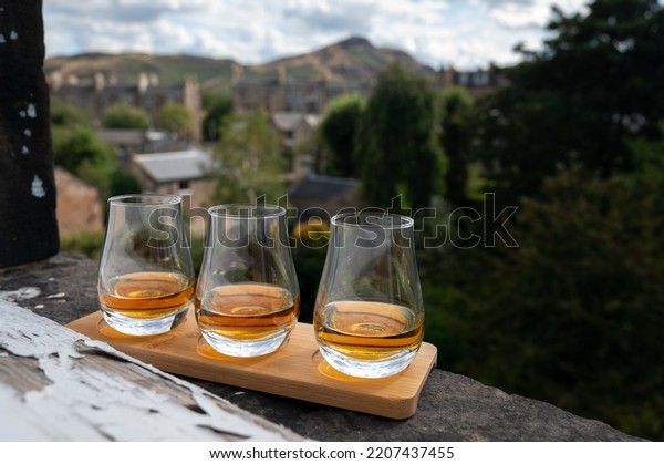 Flight of single malt scotch whisky\
served on old window sill in Scottisch house with view on old part\
of Edinburgh city and hills, Scotland, UK, dram of\
whiskey