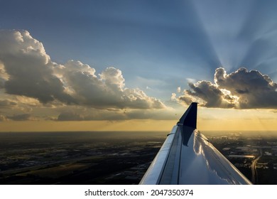 Flight wing of plane over dramatic white fluffy clouds on blue sky during sunset.