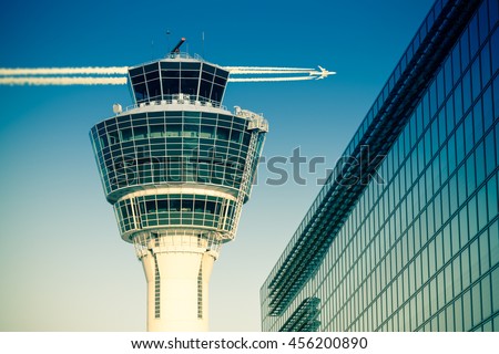 Flights management air control tower and passenger terminal in Munich international airport with flying plane in clear sky. Stock photo with split toning effect.