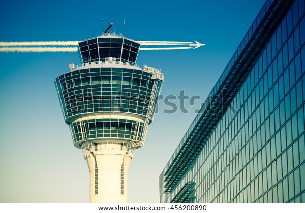 Flights management air control\
tower and passenger terminal in Munich international airport with\
flying plane in clear sky. Stock photo with split toning\
effect.