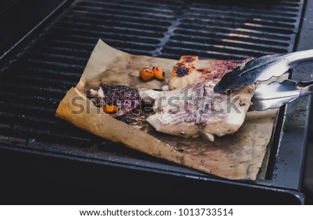 Flip the fish on the grill. The process of Barbecuing fish. Fish steak fried on grey paper.