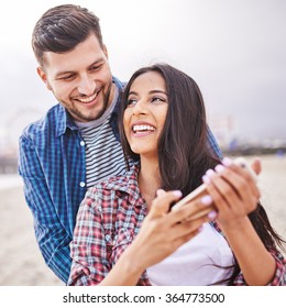 flirting hispanic couple with smartphone in square composition with selective focus
