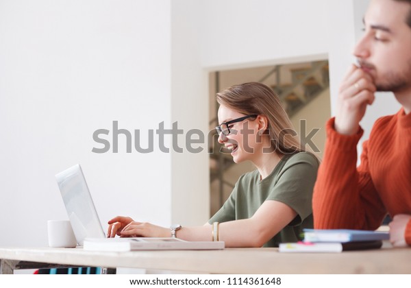 Flirting at work. Employees of an office or\
a printing house - charming woman and handsome man flipping through\
a book sitting at a table with\
computer