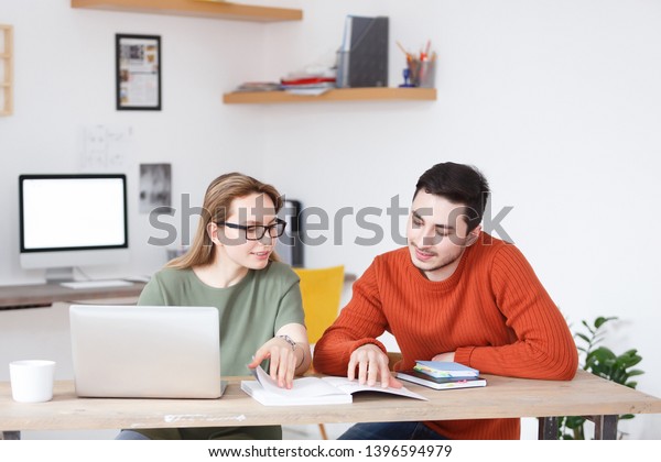Flirting at work. Employees of an office or\
a printing house - charming woman and handsome man flipping through\
a book sitting at a table with\
computer