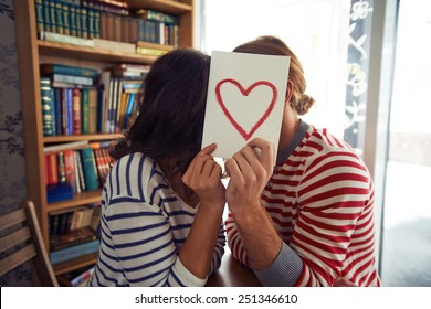 Flirty Couple Sitting In Library Behind Paper With Red Heart