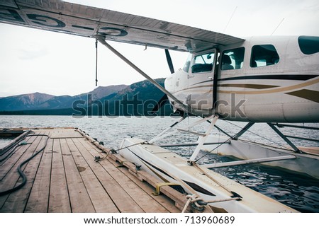 Float plane attached to a dock. Cloudy day. Mountains in the background. Landscape.