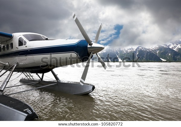 Float plane or seaplane in Alaska that has landed\
with storm clouds overhead.  The blue and white plane flew from\
Juneau.