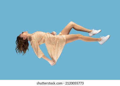 Floating in air. Relaxed girl   levitating keeping eyes closed, sleeping while flying mid-air, having comfortable peaceful dream. full length studio shot isolated on blue background, indoor