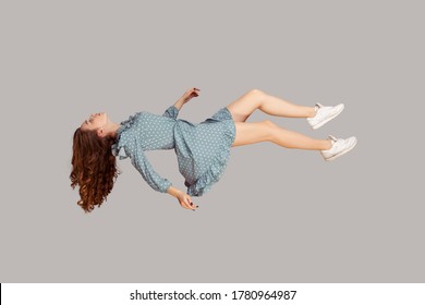 Floating in air. Relaxed girl in vintage ruffle dress levitating keeping eyes closed, sleeping while flying mid-air, having comfortable peaceful dream. full length studio shot isolated on gray, indoor