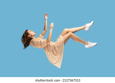 Floating in air. Relaxed girl in yellow dress levitating, looking up while flying mid-air, having comfortable peaceful dream. full length studio shot isolated on blue background, indoor