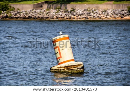floating bouy in lake saying Keep Right bobbing on rough water with relfection and blurred shore and rip rap in distance