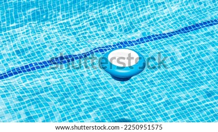 Floating dispenser in the pool with a chlorine tablet inside to correct the ph of the water before swimming. Blue and white chemical dosing float for chlorine tablets