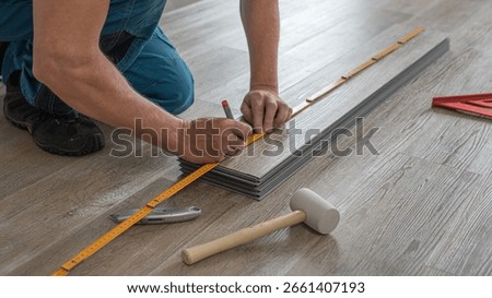 Floating floor work. The worker measuring the board of vinyl plank before shortening.