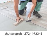 Floating floor work. The worker taps the board of vinyl plank to lock the click system. He is using hammer and wooden plank.