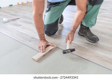 Floating floor work. The worker taps the board of vinyl plank to lock the click system. He is using hammer and wooden plank.