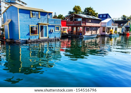 Floating Home Village Blue Red Brown Houseboats Fisherman's Wharf Reflection Inner Harbor, Victoria British Columbia Canada Pacific Northwest.  Area has floating homes, boats, piers, and restaurants. 