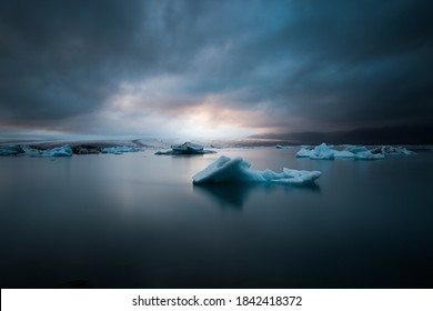 Floating Ice and Icebergs in a glacier lake in Iceland with a sunset breaking through the dark clouds in the background.  - Powered by Shutterstock