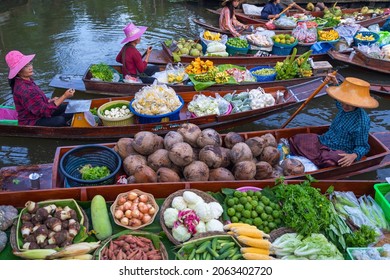 Floating Market tourists visiting by boat popular attractions on canals of Ratchaburi, Thailand. Merchant sell fruits, agricultural produce, and Thai cuisine on the wooden boat.