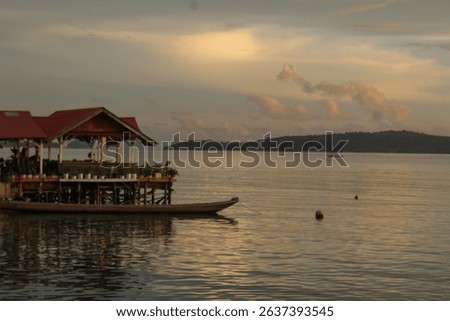 A floating restaurant sits peacefully on calm water reflecting the sunset sky and distant island view suggesting relaxing tropical travel.