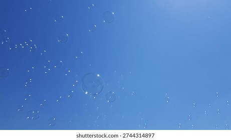 Floating soap bubbles against a clear blue sky with soft sunlight reflections. Minimal summer background with copy space, symbolizing freedom, freshness, purity, and dreamy atmosphere.