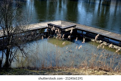 floating walkway made of wooden planks, pier, narrow curved paths on stilts driven to the bottom above the lake water. has no railings. more design sidewalk with low railings for wheelchairs