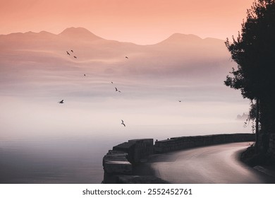 Flock of birds flying over misty sea at sunset with winding road and mountains in background - Powered by Shutterstock