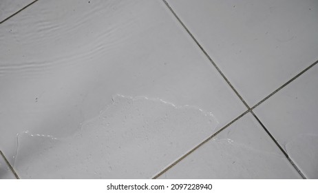 Flood Clean Water Flows Over White Ceramic Tile Covering Floor At Home Because Of Hard Pipe Damage In Bathroom Close Upper View.