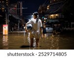 flood victims woman stands in the flooded streets of Chiang Mai city at night 2024, holding a bag with personal belongings. Another person wades ahead through the water