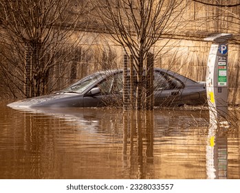 A flooded carpark showing a partially submerged car next to a ticket machine