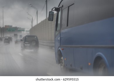 Flooded City Road With Rain Puddles And With Riding Cars Splashing Water From The Wheels. Big Blue Bus.