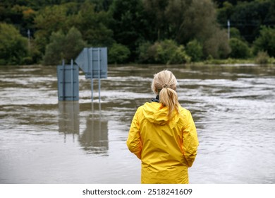 Flooded river. Worried woman looking at overflowing water during flood. Extreme weather and natural disaster