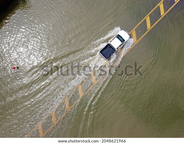 Flooded roads, people with cars running through.\
Aerial drone photography shows streets flooding and people\'s cars\
passing by, splashing\
water.