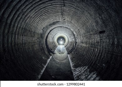 Flooded round underground drainage sewer tunnel with dirty sewage water in counter-light