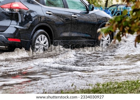 Flooding in the city after the rain. The car drives through a puddle in the pouring rain. Splashes of water from under the wheels of the car. Transport collapse. Severe weather conditions