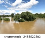 Flooding of the Grand River, Brantford, Ontario, Canada. Looking down from Cockshutt Road Bridge. Blue sky clouds. Muddy fast moving water. Flood flooded. After the rain. Force of nature. Trees field.