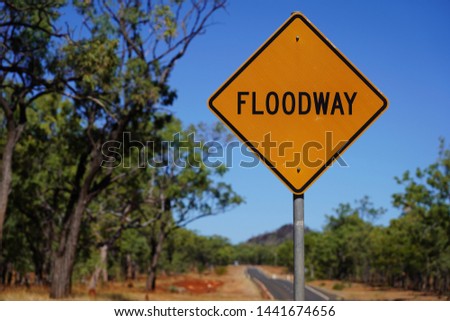 Floodway - warning sign in the Australian Outback. Surrounded by a dusty road and some green trees.