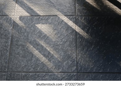 Floor features bold diagonal shadows from a railing, creating a moody geometric composition. The interplay of light and texture evokes urban architecture and a calm, cool ambiance.