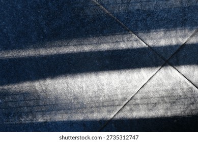 Floor features bold diagonal shadows from a railing, creating a moody geometric composition. The interplay of light and texture evokes urban architecture and a calm, cool ambiance.