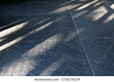 Floor features bold diagonal shadows from a railing, creating a moody geometric composition. The interplay of light and texture evokes urban architecture and a calm, cool ambiance.